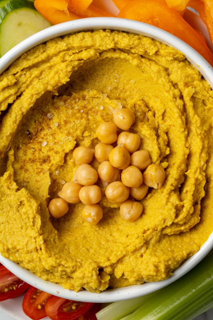 curry hummus in white bowl topped with chickpeas and salt