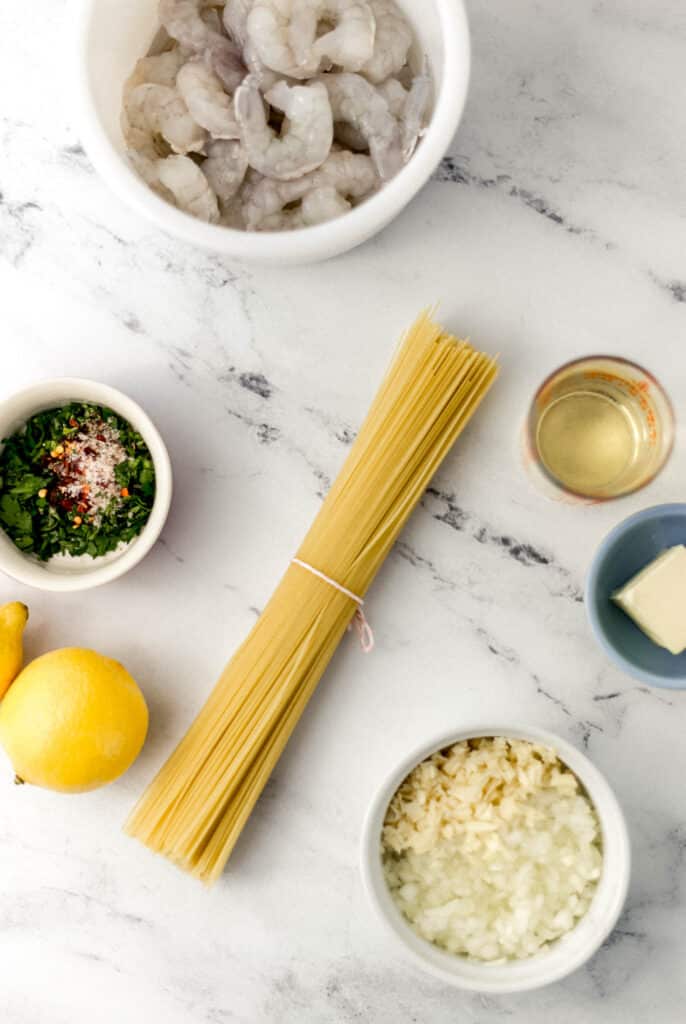 ingredients needed to make shrimp scampi in separate containers on marble surface