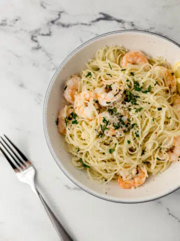overhead view of bowl of easy shrimp scampi topped with parsley beside a fork.