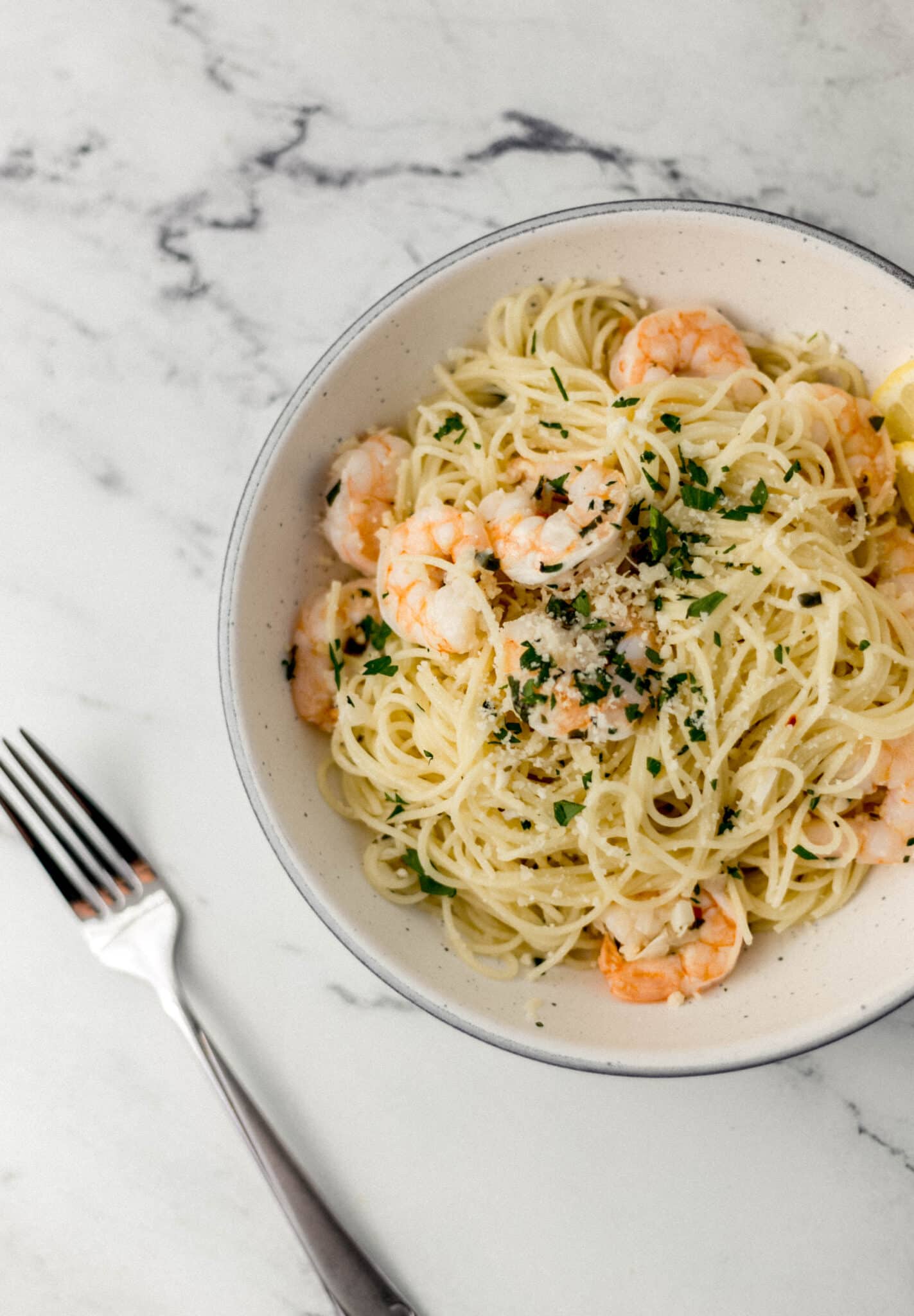 overhead view of bowl of easy shrimp scampi topped with parsley beside a fork.