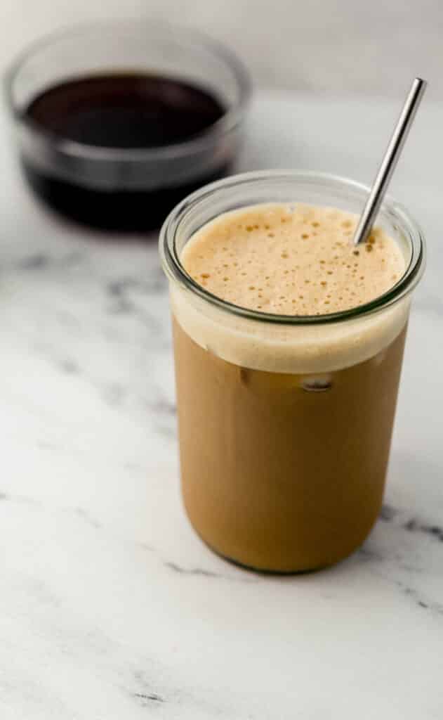 close up side view of iced espresso drink with brown sugar syrup in glass bowl in background