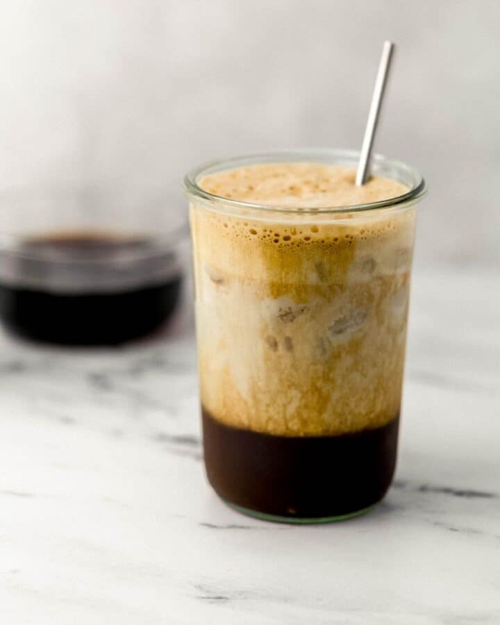Milk added to espresso drink in glass with straw. 
