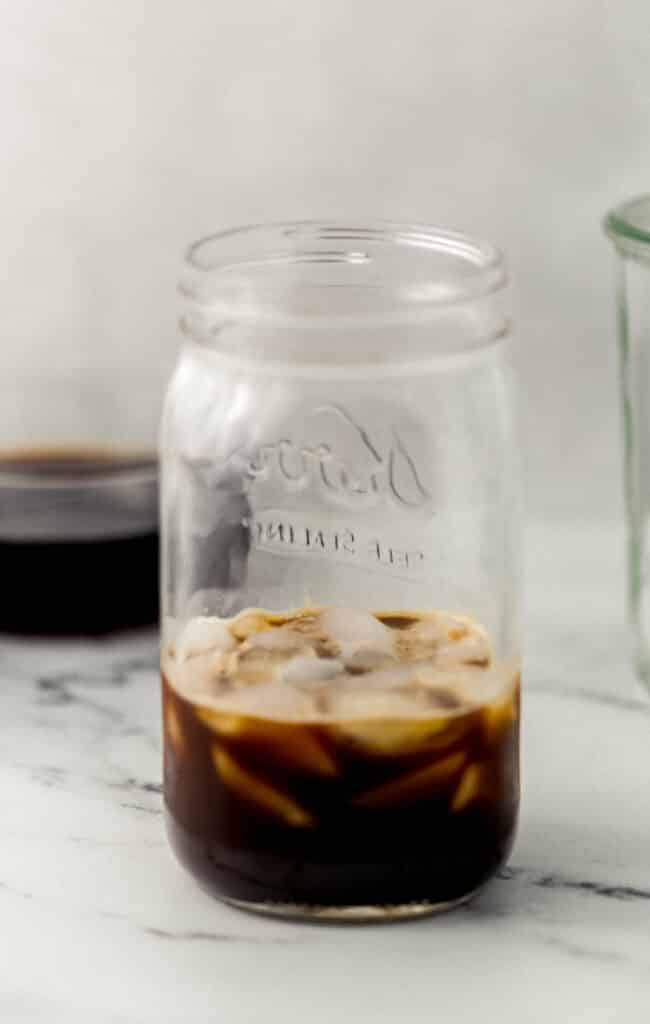 close up side view of glass jar with ice, espresso, and syrup in it. 