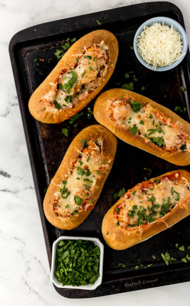 sheet pan with four meatball subs topped with cheese and parsley