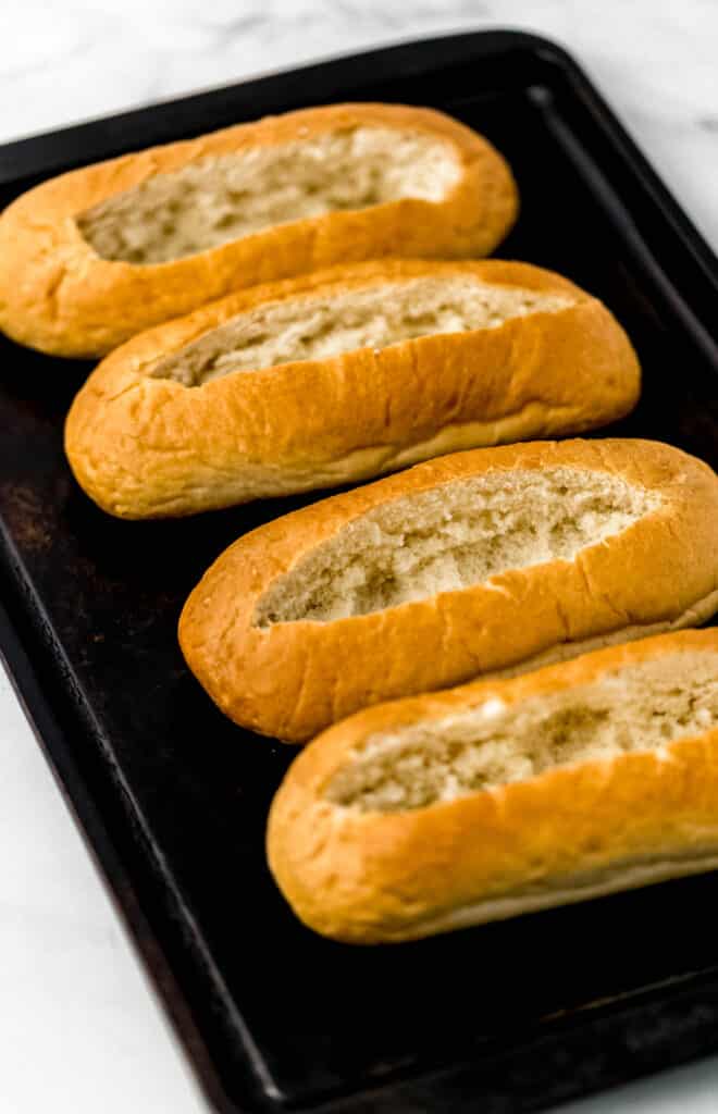 sheet pan with hoagie buns on it with the top cut out. 