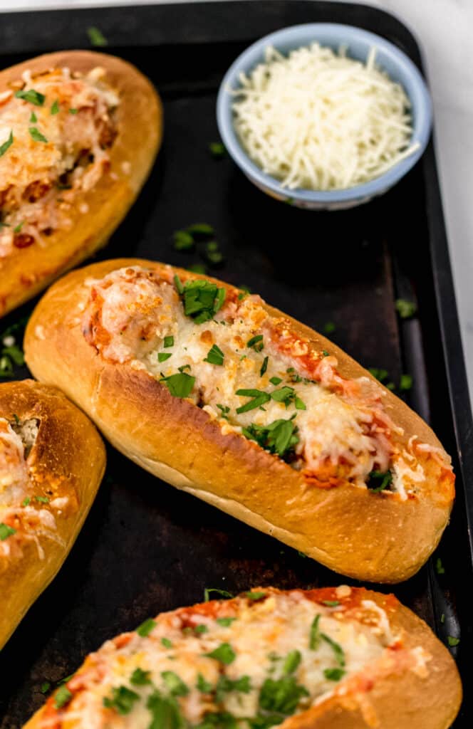 meatball subs on sheet pan topped with shredded cheese and fresh parsley
