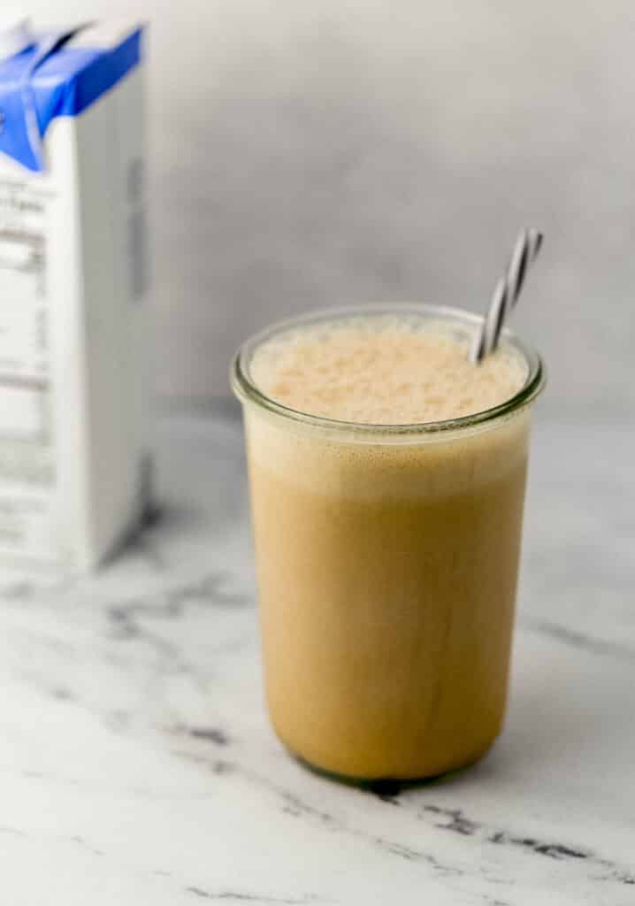 close up side view of almond milk frappe in glass with straw with carton of almond milk in the background