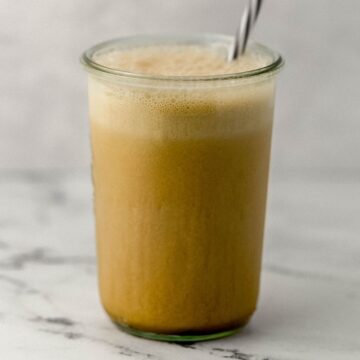 Front view of frappuccino in tall glass with straw in it on marble surface.