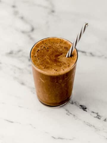 mocha smoothie in glass on marble surface with straw in it