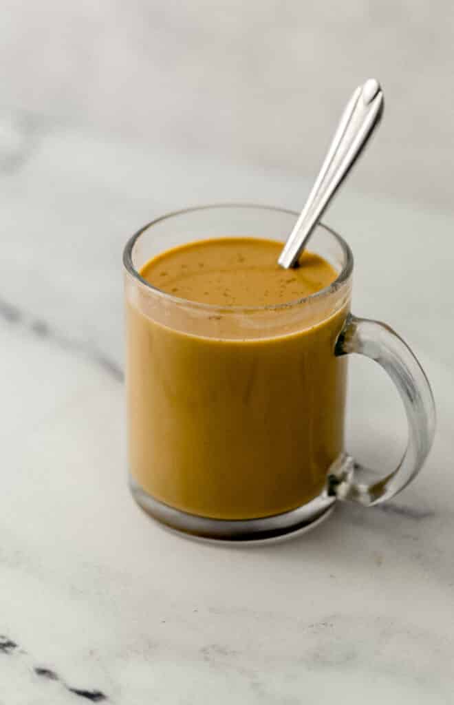 close up side view of glass mug with latte ingredients combined with spoon