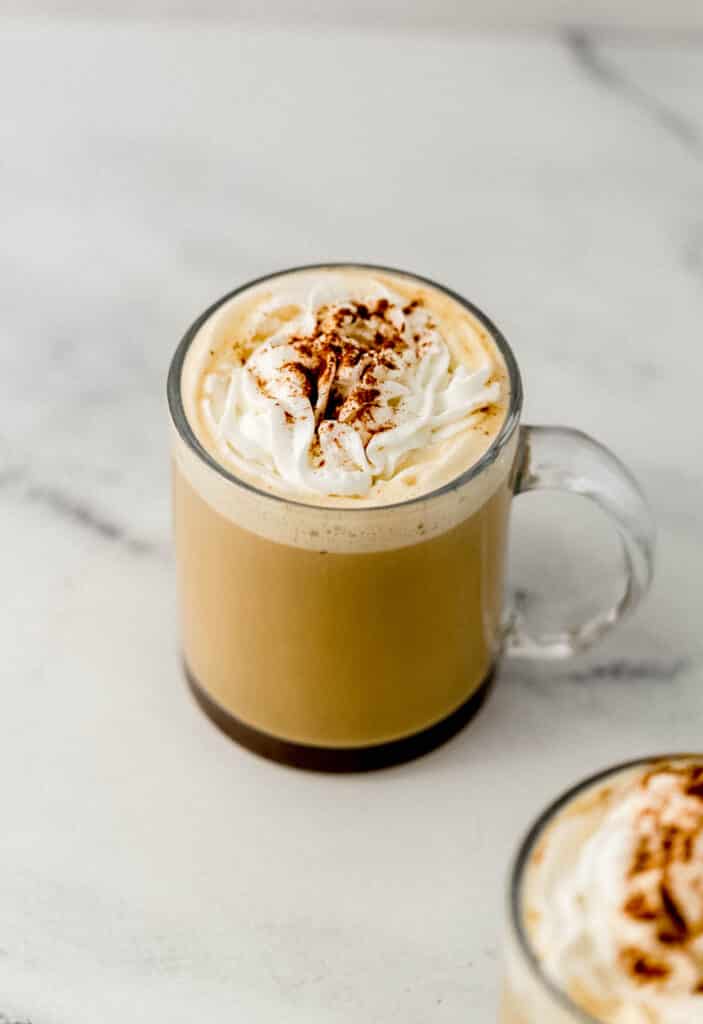 latte in glass mug topped with whipped cream and a sprinkle of ground cinnamon 