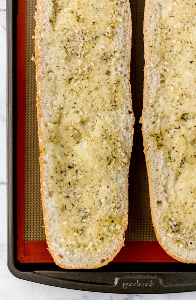 French bread on sheet pan with garlic butter sauce on it.