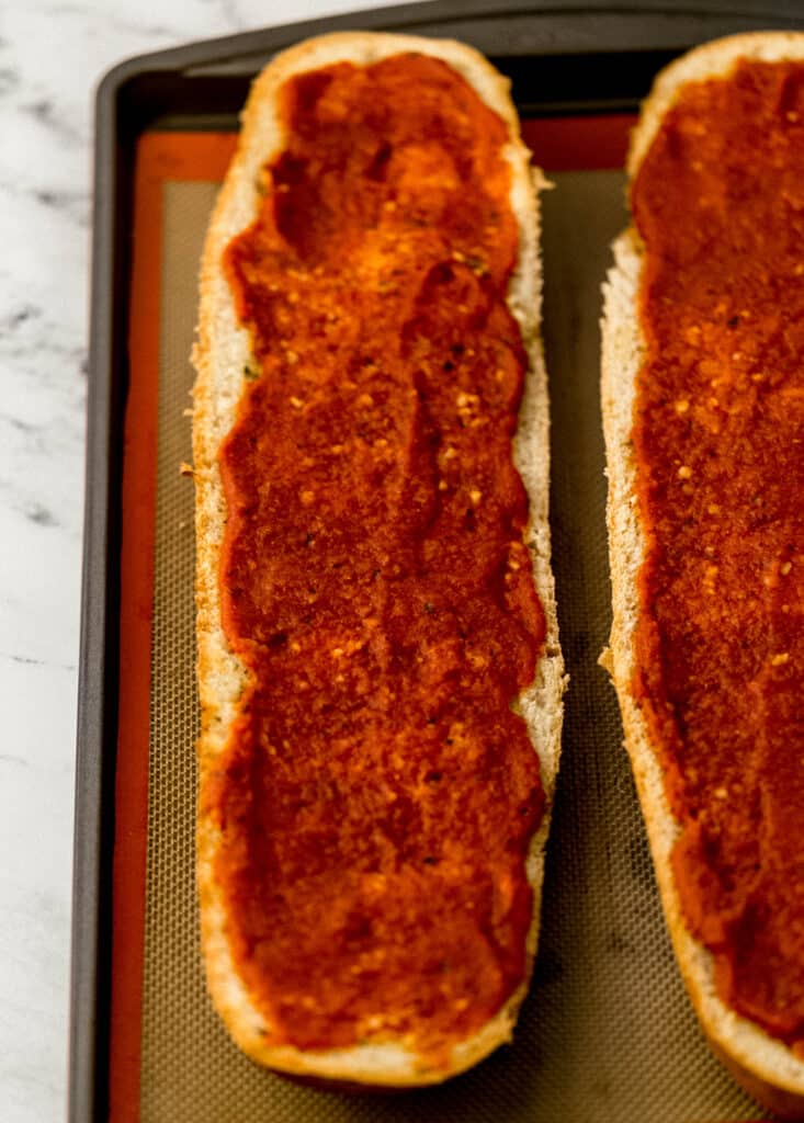 sauce spread on French bread on sheet pan