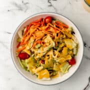overhead view of white bowl of salad topped with dressing next to fork and jar of dressing