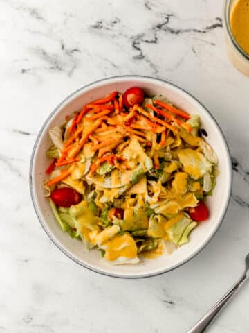 overhead view of white bowl of salad topped with dressing next to fork and jar of dressing