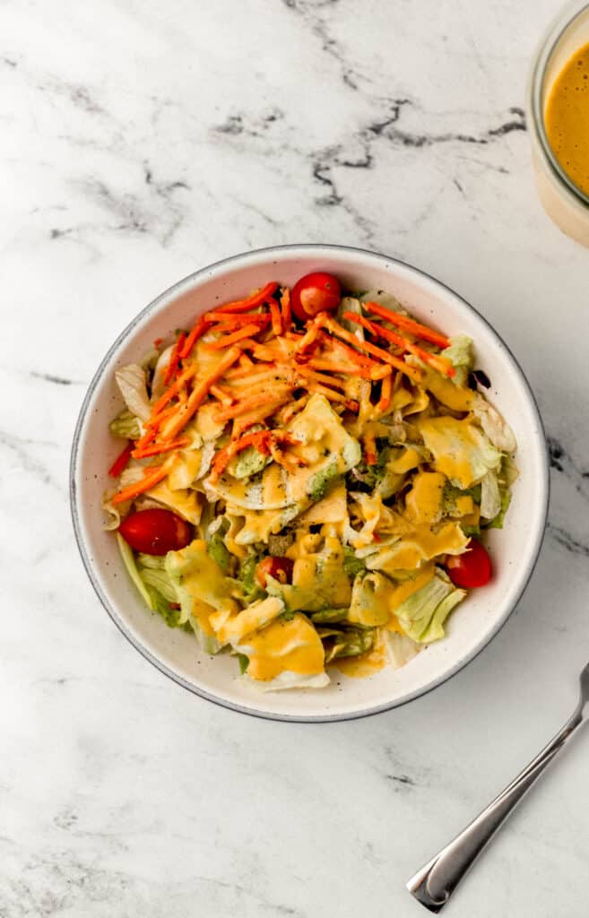 overhead view of white bowl of salad topped with dressing next to fork and jar of dressing