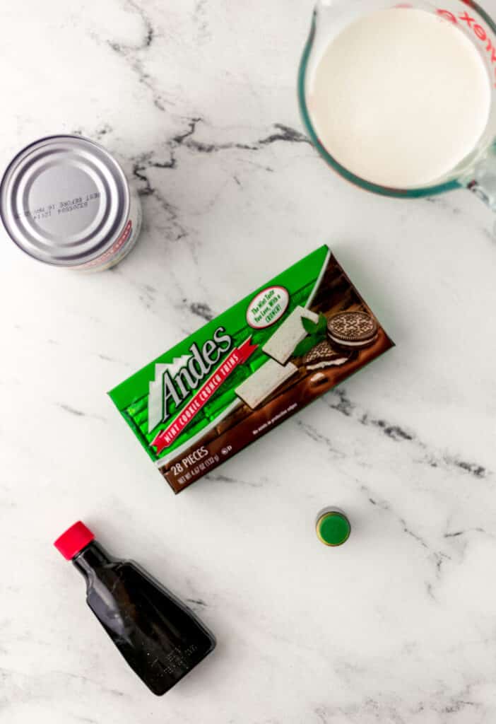 ingredients needed to make homemade mint chocolate ice cream on marble surface.