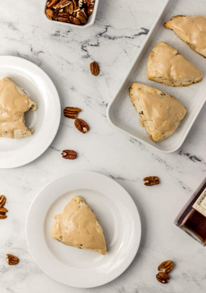 overhead view of maple pecan scones on white plates and a platter with a small container of pecans and maple syrup