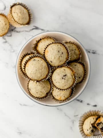Mexican chocolate banana muffins in gold liners inside a white bowl on a marble surface