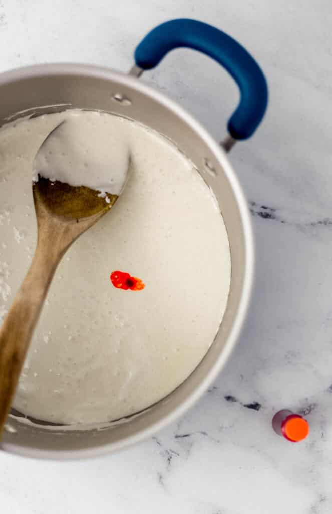 melted marshmallows, butter, and orange food coloring in pot with wooden spoon. 