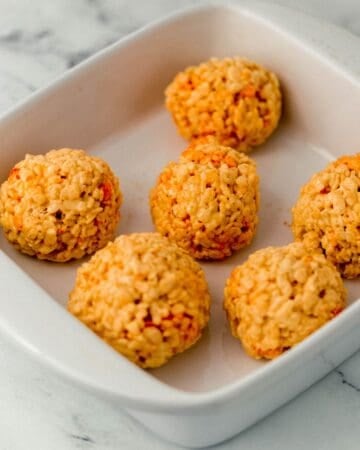 Orange ball shaped rice krispie treats in white baking dish.
