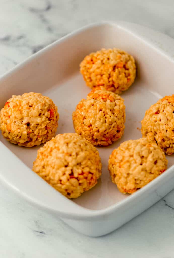 rice krispie treat mixture rolled into orange balls in white baking dish