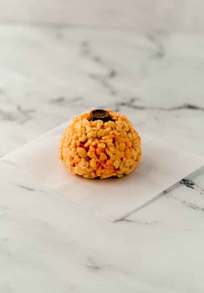 close up side view pumpkin shaped rice krispie treat with chocolate in the top