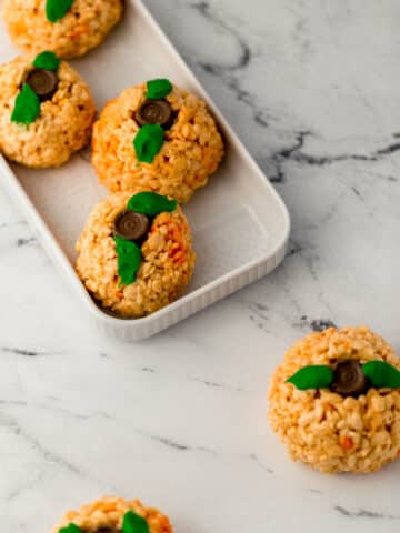 pumpkin shaped rice krispie treats on rectangle platter and marble surface