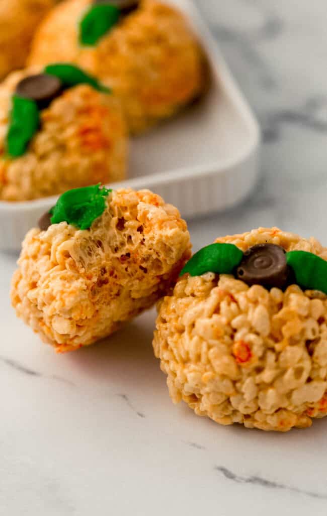 pumpkin shaped rice krispie treat with bite in it next to a finished one