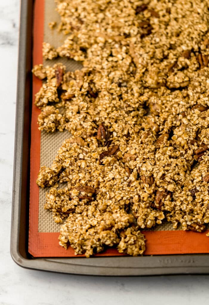 uncooked granola spread out on baking sheet lined with reusable liner 