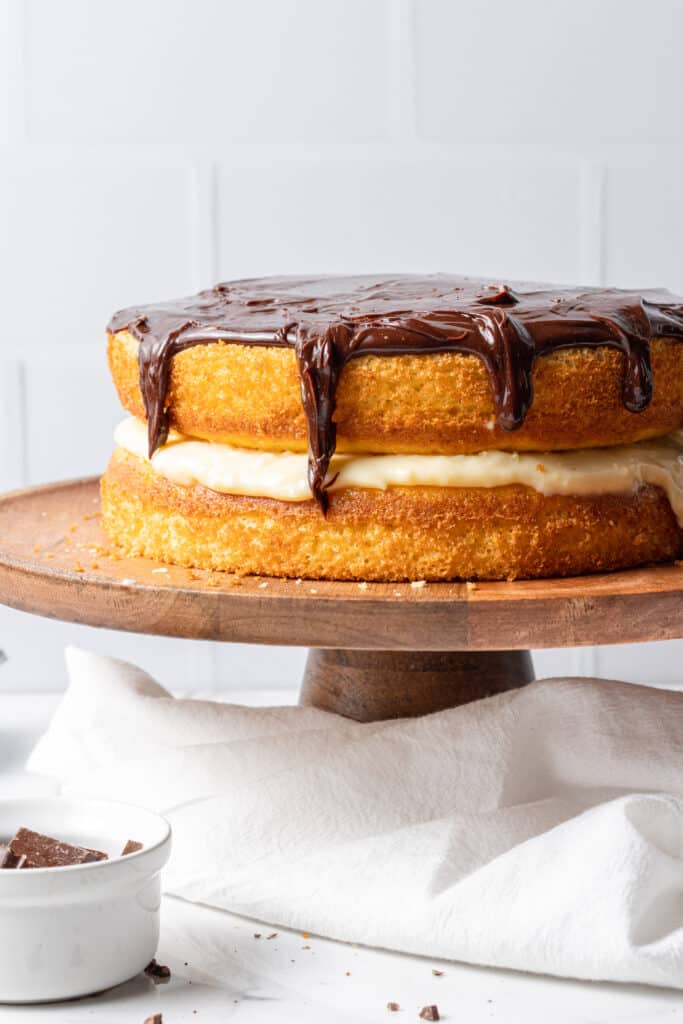 close up side view of Boston cream cake on wooden cake stand with cloth napkin 