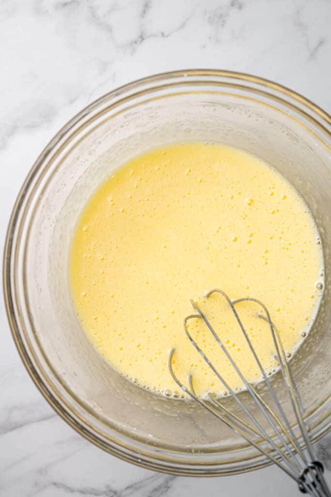 glass mixing bowl with whisk and ingredients to make pastry cream in it. 