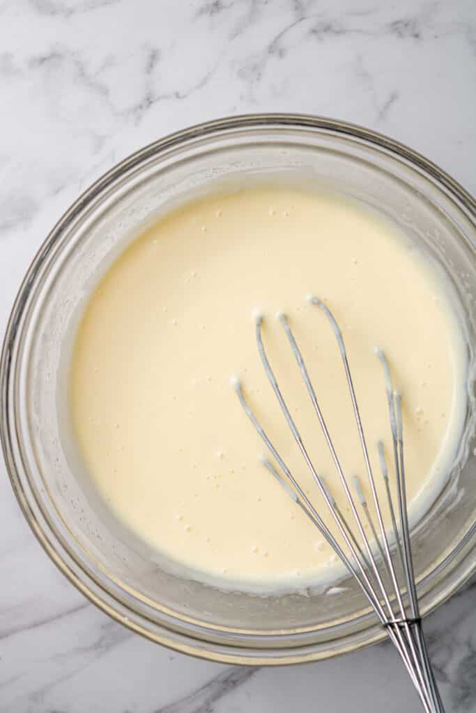 strained pastry cream in glass mixing bowl with whisk.