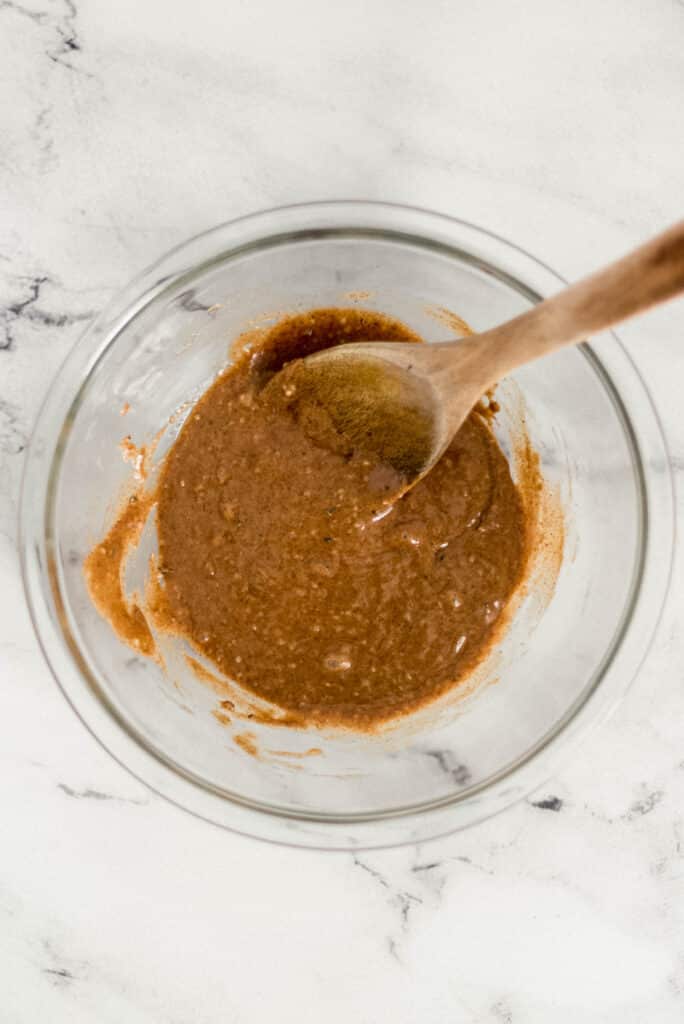 almond butter, honey, hemp seeds, and vanilla extract combined in glass mixing bowl with wooden spoon 