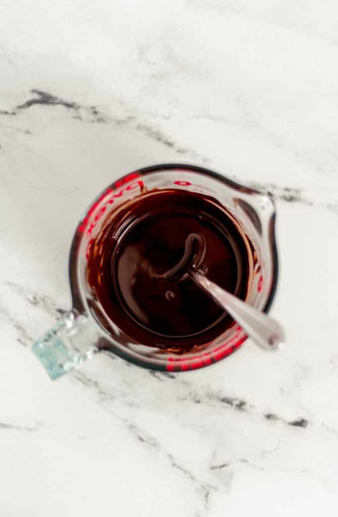 chocolate and coconut oil combined in pyrex pitcher with spoon