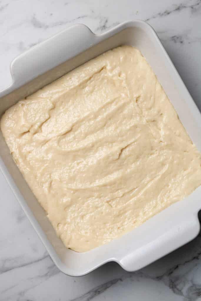 cinnamon roll cake mixture spread evenly in white square baking dish 