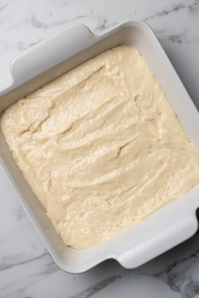 cinnamon roll cake mixture spread evenly in white square baking dish 