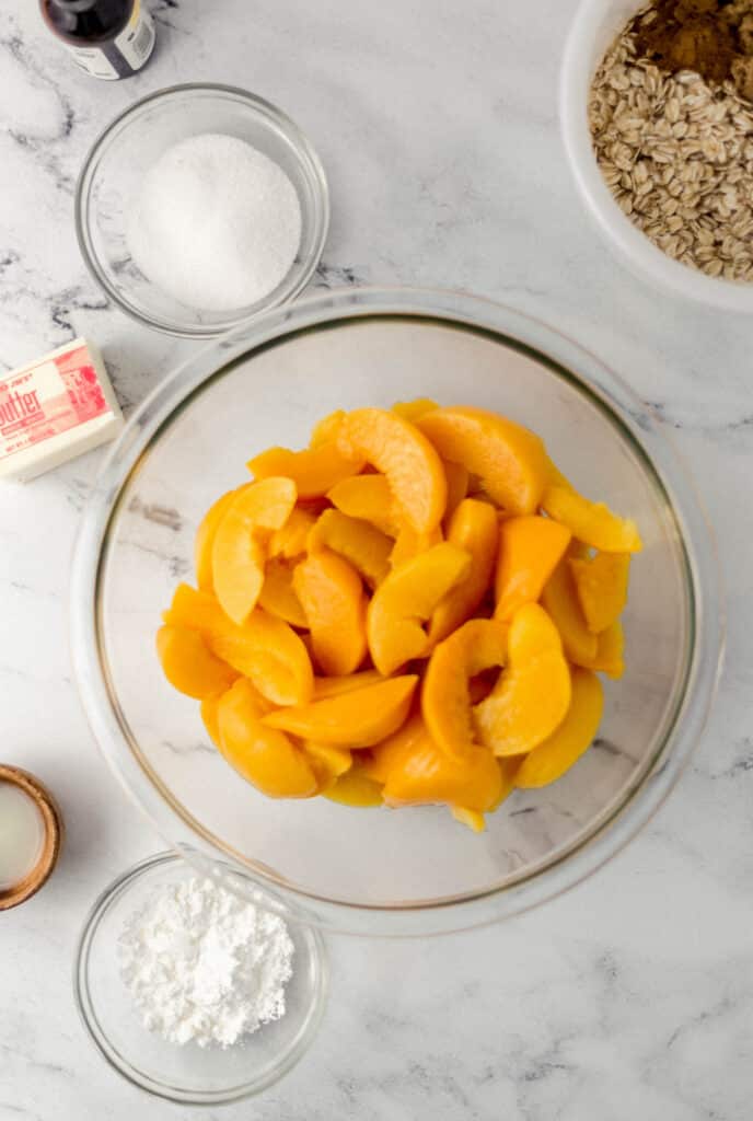 ingredients needed to make peach crisp in separate containers on marble surface 