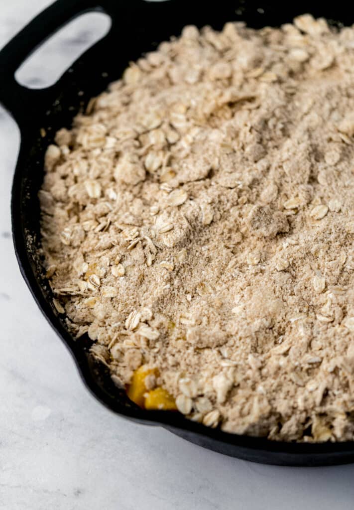 close up side view of unbaked peach crisp in cast iron skillet