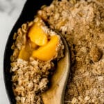 easy cling peach crisp in cast iron skillet with wooden spoon