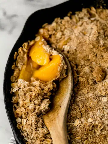 easy cling peach crisp in cast iron skillet with wooden spoon