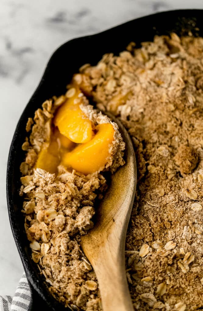 easy cling peach crisp in cast iron skillet with wooden spoon