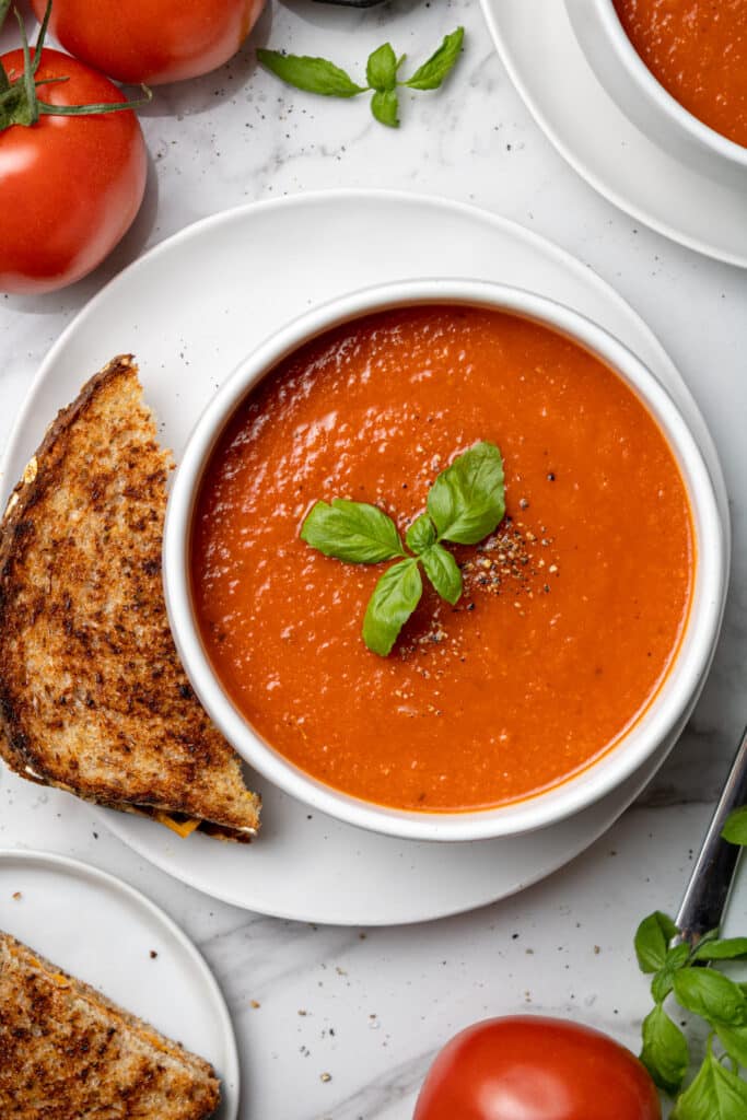 overhead view tomato soup in white bowl with grilled cheese sandwich on the side