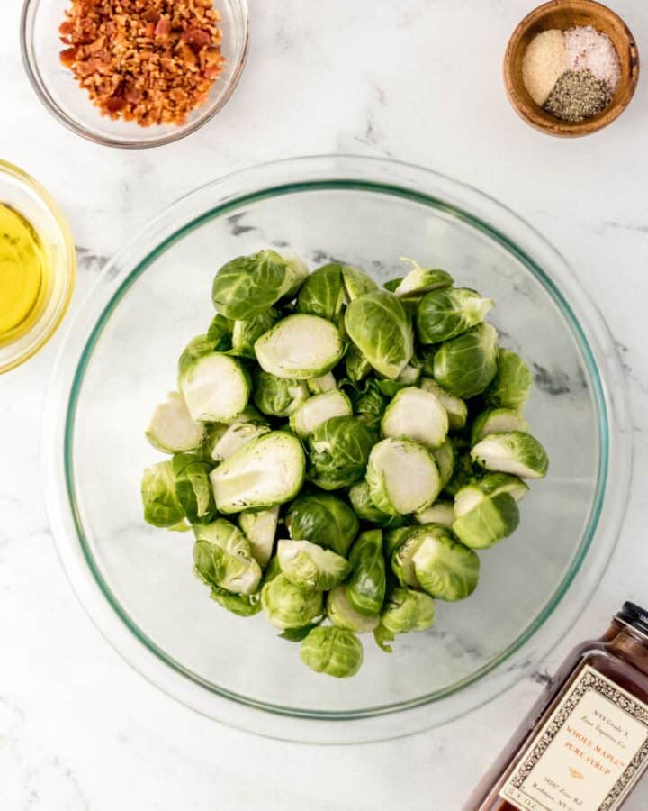 Overhead view of ingredients needed to make brussels in separate bowls on marble surface. 