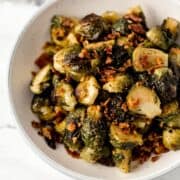 Close up overhead view of finished brussel sprouts and bacon in white bowl.