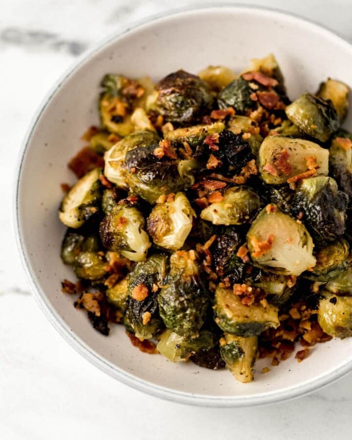 Close up view of finished brussel sprouts in white bowl on marble surface. 