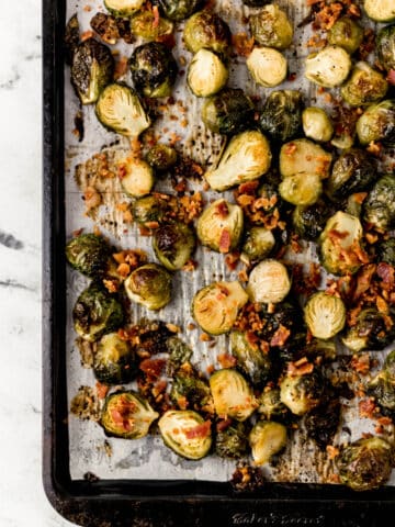 overhead view maple roasted brussels sprouts topped with bacon on parchment lined baking sheet