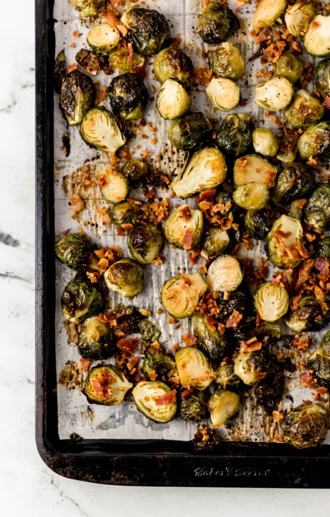 overhead view roasted brussels sprouts topped with bacon on parchment lined baking sheet