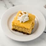 side view square slice on pumpkin cheesecake on white plate topped with whipped topping