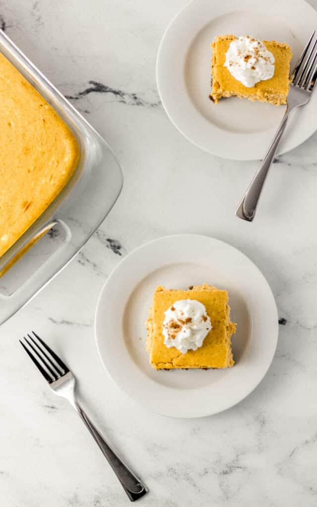 overhead view of pumpkin cheesecake on two white plates with forks and in glass baking dish